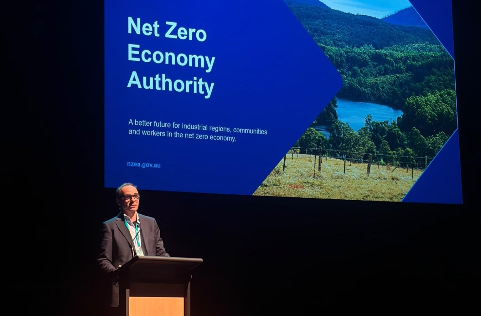 NZEA CEO David Shankey standing at a lectern in front of a PowerPoint presentation