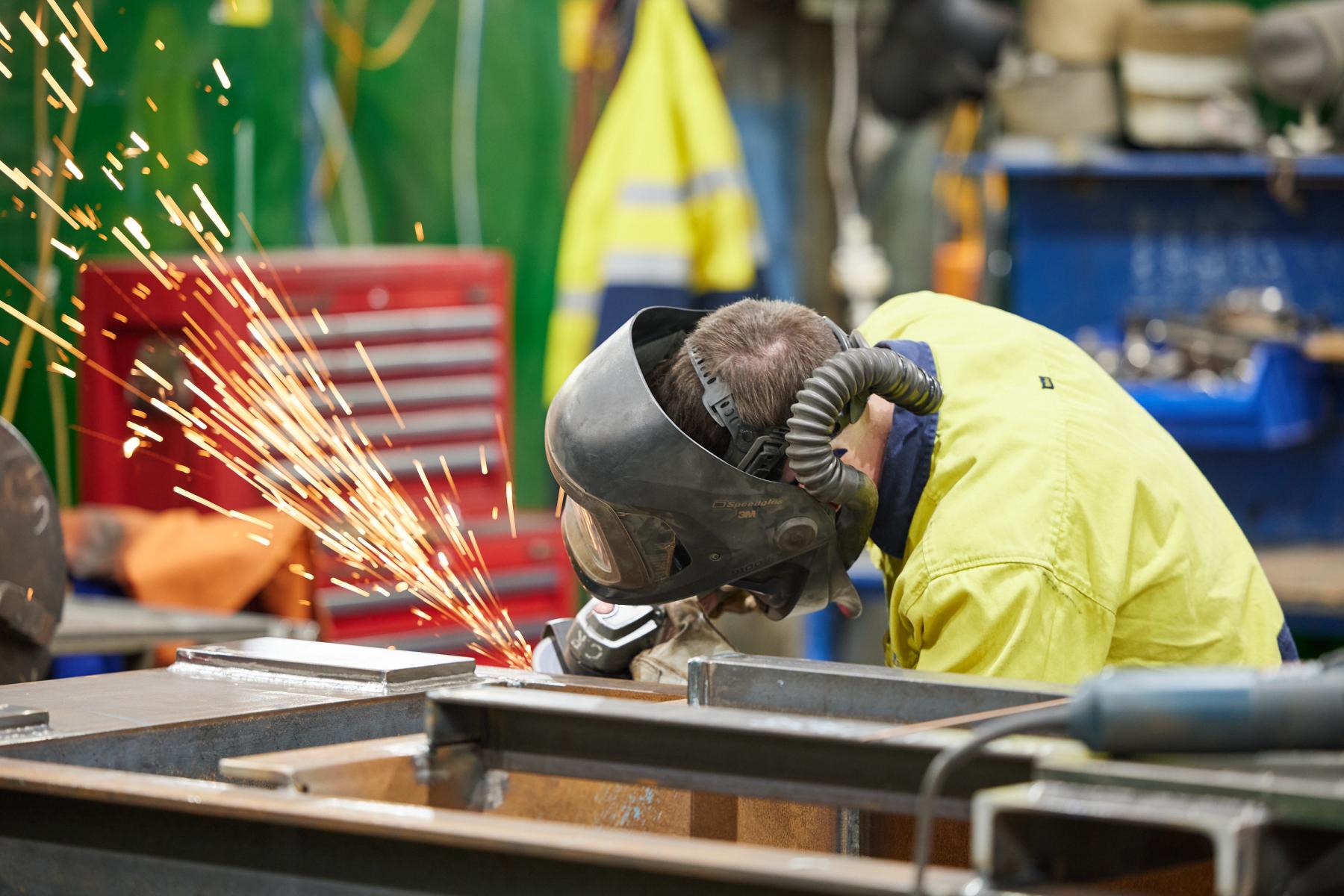 A man in a welding mask using an angle grinder