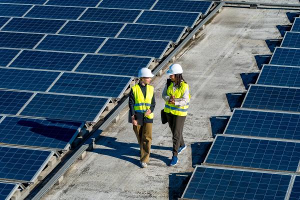 Two women in high-vis safety gear walking between two fields of solar panels.